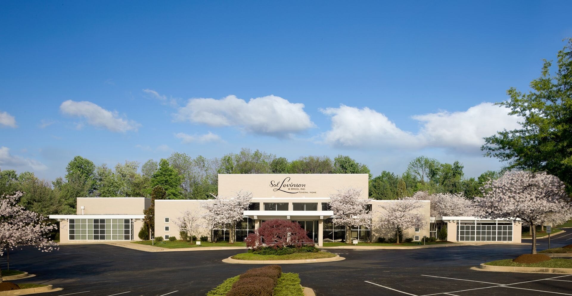Sol Levinson funeral home in Pikesville beneath a wide spring sky, framed by cherry blossoms